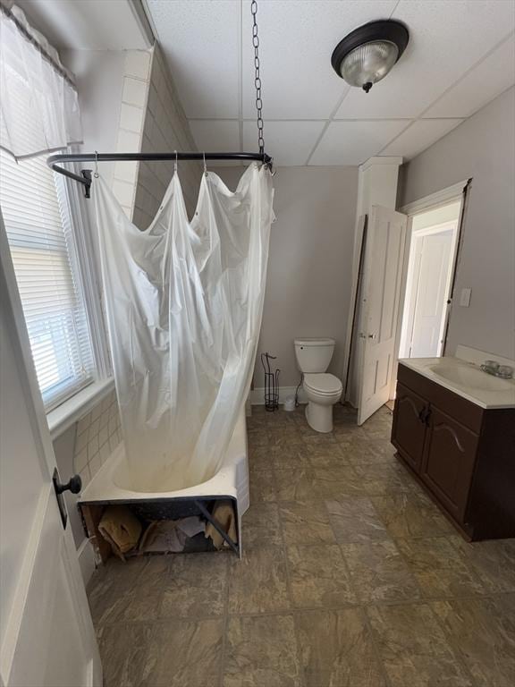 bathroom with a drop ceiling, vanity, toilet, and shower / bath combo with shower curtain