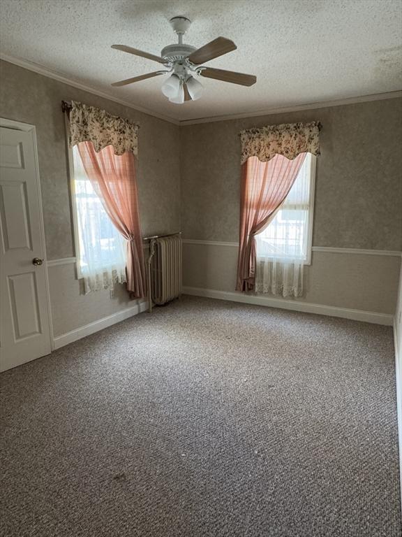 carpeted spare room featuring wallpapered walls, radiator heating unit, ceiling fan, ornamental molding, and a textured ceiling