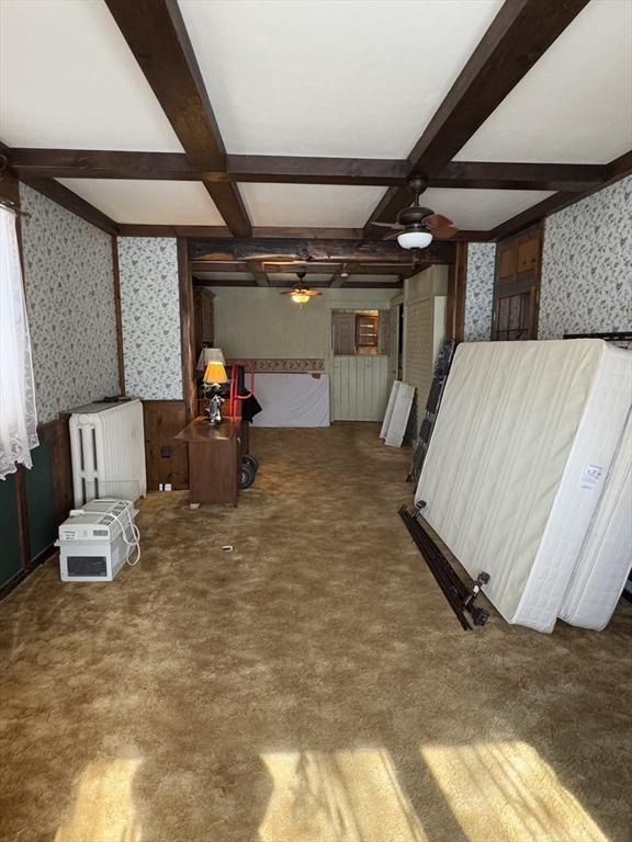 living area featuring radiator, coffered ceiling, beamed ceiling, and wallpapered walls