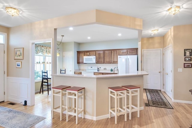 kitchen with a kitchen breakfast bar, backsplash, white appliances, light hardwood / wood-style floors, and an island with sink