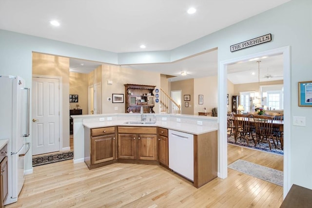 kitchen featuring kitchen peninsula, light wood-type flooring, white appliances, sink, and pendant lighting