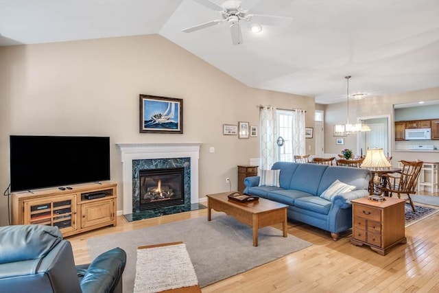 living room featuring ceiling fan with notable chandelier, lofted ceiling, a high end fireplace, and light hardwood / wood-style flooring