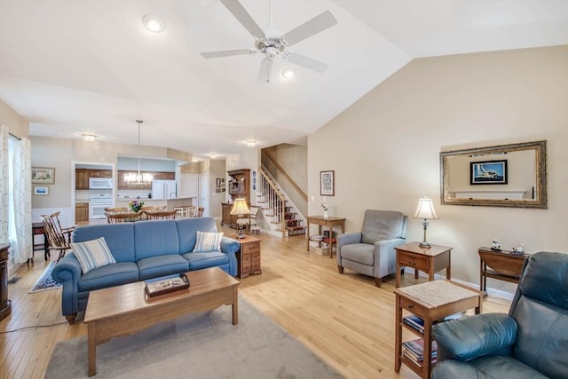 living room with ceiling fan with notable chandelier, light hardwood / wood-style floors, and lofted ceiling