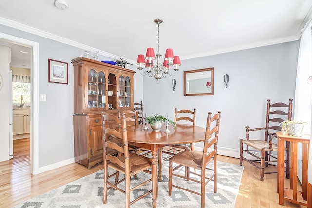 dining space with a notable chandelier, light hardwood / wood-style flooring, crown molding, and sink