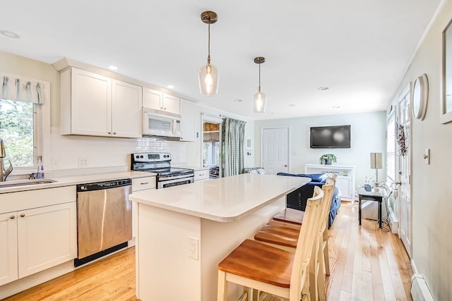 kitchen featuring pendant lighting, light wood-type flooring, sink, a kitchen island, and appliances with stainless steel finishes