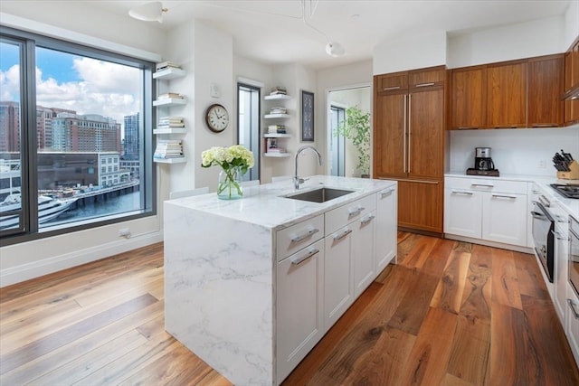 kitchen featuring sink, a center island with sink, light stone countertops, white cabinetry, and light wood-type flooring