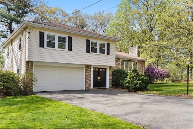 tri-level home with aphalt driveway, a chimney, a garage, brick siding, and a front lawn