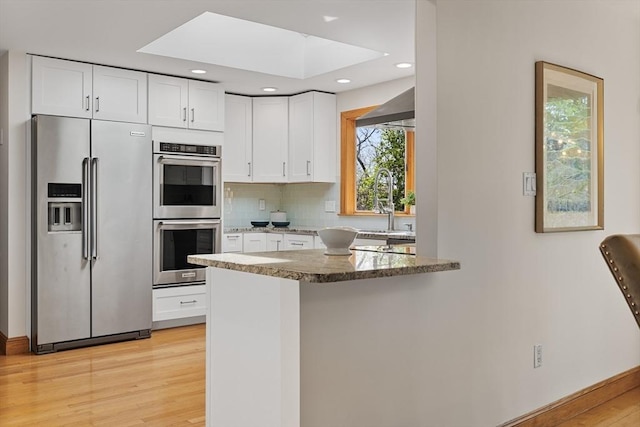 kitchen featuring light stone countertops, light wood-type flooring, white cabinetry, tasteful backsplash, and stainless steel appliances