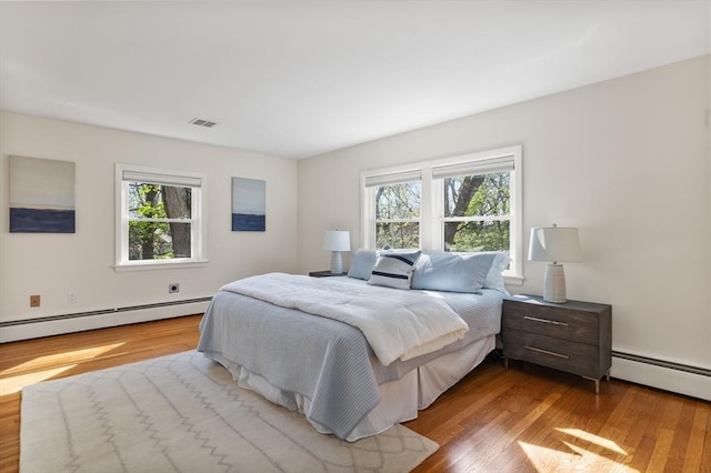 bedroom featuring a baseboard radiator, multiple windows, and wood finished floors