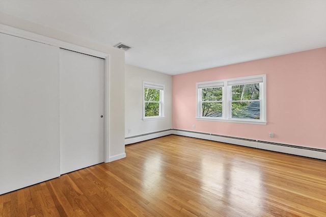unfurnished bedroom featuring a closet, a baseboard heating unit, wood finished floors, and visible vents