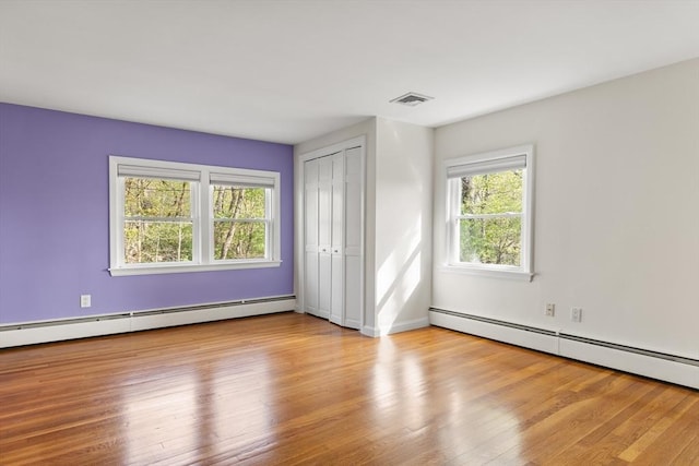 unfurnished bedroom featuring a baseboard heating unit, baseboards, visible vents, and wood finished floors