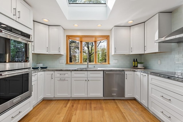 kitchen featuring decorative backsplash, wall chimney exhaust hood, appliances with stainless steel finishes, and white cabinetry