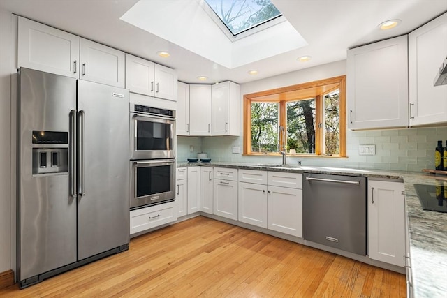 kitchen featuring a skylight, tasteful backsplash, a sink, white cabinets, and stainless steel appliances