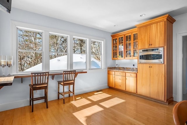 kitchen with plenty of natural light, stainless steel oven, light wood-style flooring, and baseboards