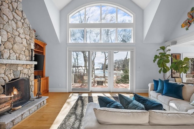 living room with high vaulted ceiling, light wood-style flooring, a fireplace, and baseboards