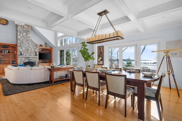 dining room with beam ceiling, crown molding, a stone fireplace, light wood-type flooring, and coffered ceiling