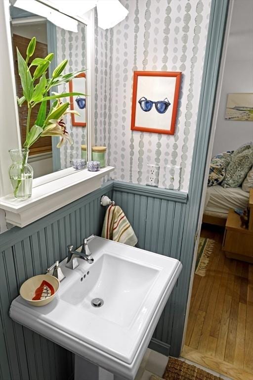 bathroom featuring hardwood / wood-style floors, wallpapered walls, wainscoting, and a sink