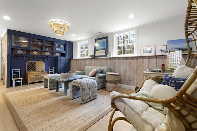 living area with wood finished floors, recessed lighting, ornamental molding, and a wainscoted wall