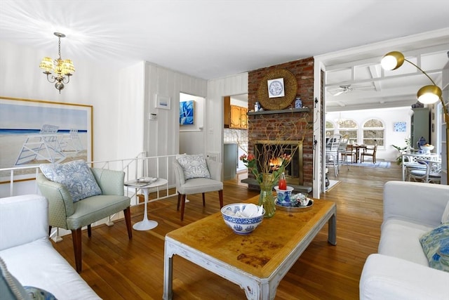 living room with a brick fireplace, wood finished floors, a ceiling fan, a chandelier, and beam ceiling