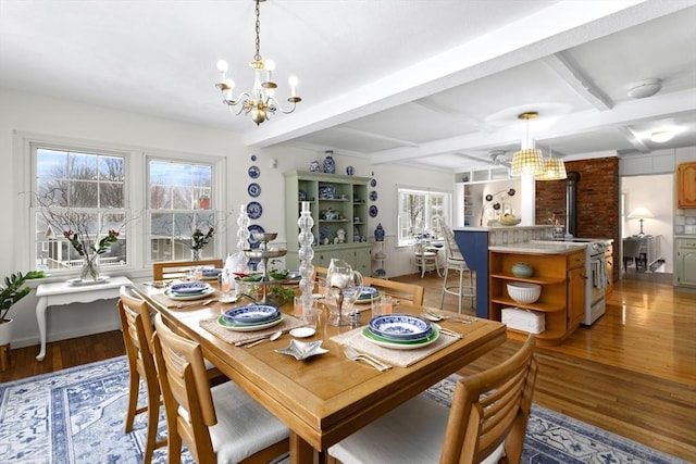 dining space with a chandelier, plenty of natural light, light wood-style flooring, a wood stove, and beam ceiling