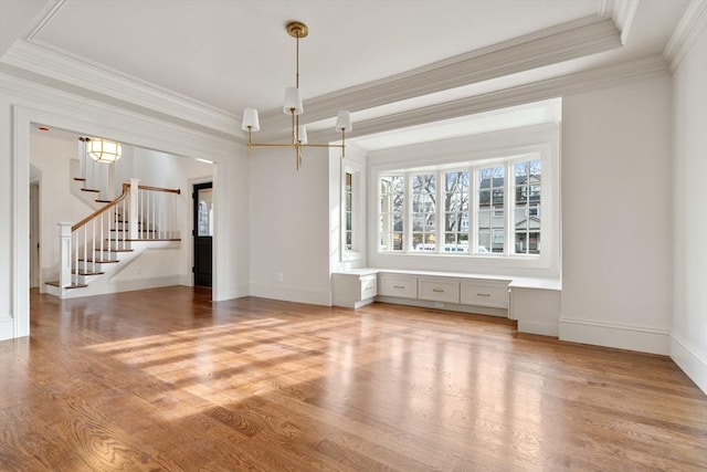 unfurnished living room featuring a raised ceiling, hardwood / wood-style floors, ornamental molding, and a notable chandelier