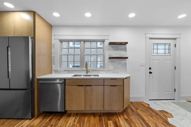 kitchen with decorative backsplash, sink, light wood-type flooring, and appliances with stainless steel finishes