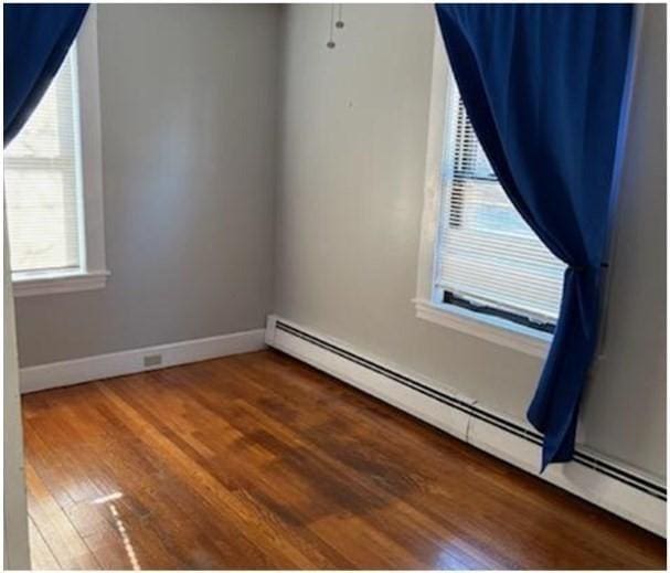 unfurnished room featuring a baseboard radiator, wood finished floors, and baseboards