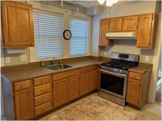 kitchen featuring stainless steel range with gas cooktop, under cabinet range hood, a sink, dark countertops, and a ceiling fan