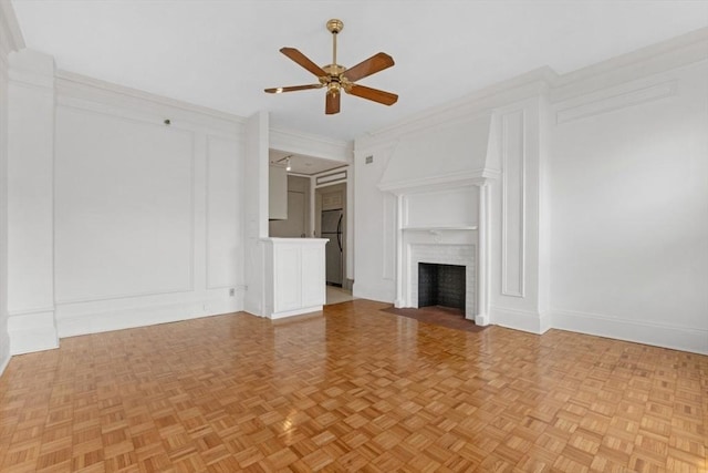 unfurnished living room with a fireplace with flush hearth, crown molding, a decorative wall, and ceiling fan