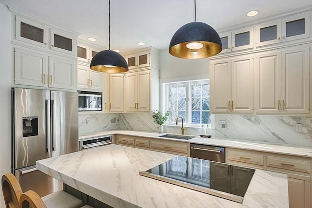 kitchen featuring hanging light fixtures, appliances with stainless steel finishes, a sink, and light stone counters