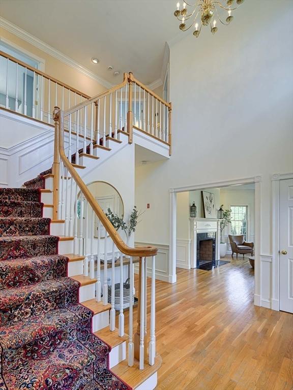 staircase with a fireplace, crown molding, a decorative wall, an inviting chandelier, and wood finished floors