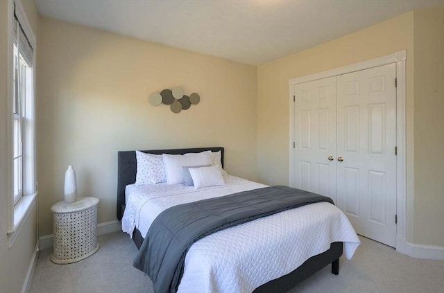 bedroom with a closet, light colored carpet, and baseboards