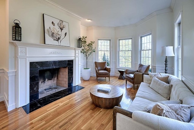 living room featuring a premium fireplace, ornamental molding, a decorative wall, and wood finished floors