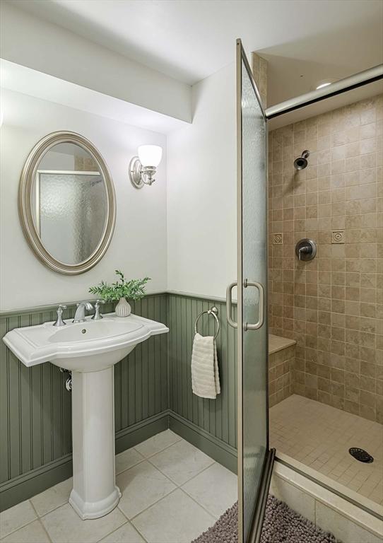 bathroom with tile patterned flooring, wainscoting, a sink, and a shower stall