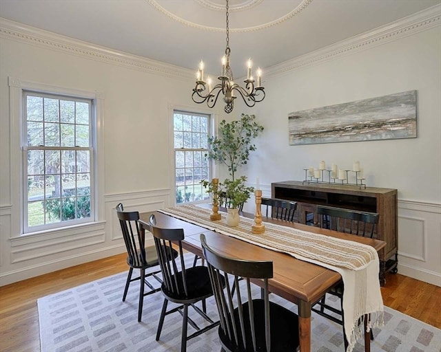 dining space featuring a decorative wall, ornamental molding, wainscoting, wood finished floors, and a chandelier