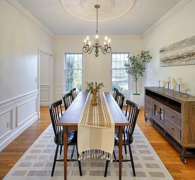 dining space with wainscoting, ornamental molding, an inviting chandelier, light wood-style floors, and a decorative wall