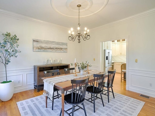 dining area with a decorative wall, light wood-type flooring, visible vents, and a notable chandelier