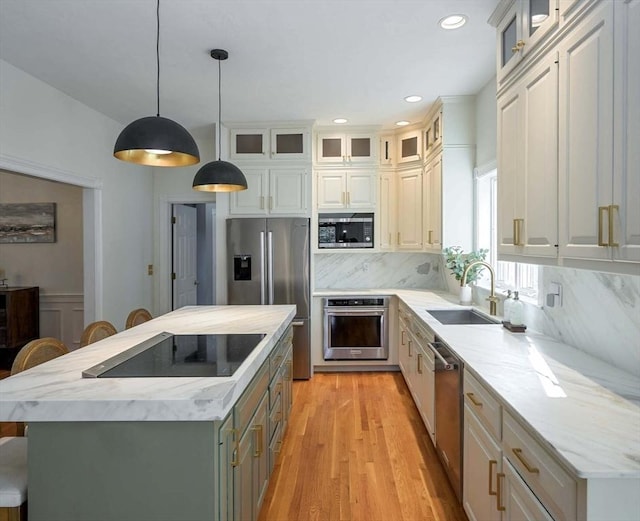 kitchen with a sink, hanging light fixtures, appliances with stainless steel finishes, a center island, and glass insert cabinets