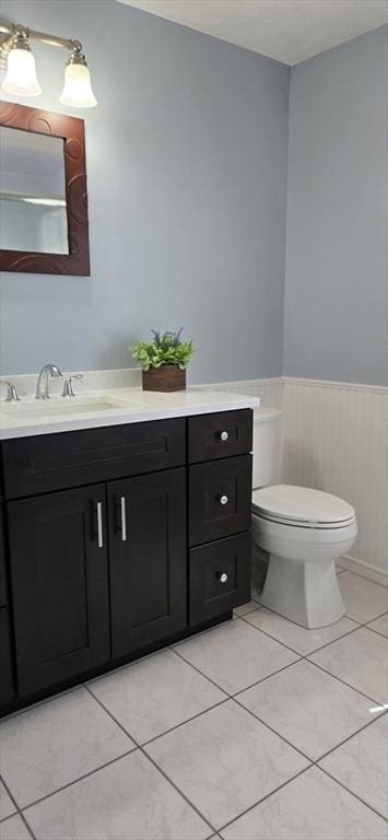 half bath featuring tile patterned floors, wainscoting, toilet, and vanity