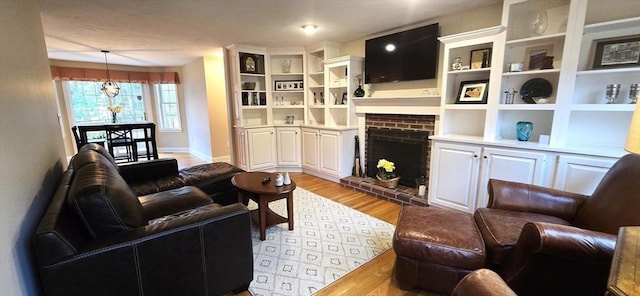 living area with a chandelier, baseboards, light wood-type flooring, a fireplace, and built in shelves