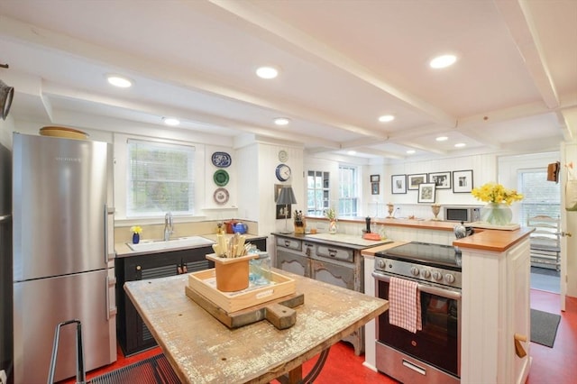 kitchen with appliances with stainless steel finishes, butcher block counters, sink, kitchen peninsula, and beam ceiling