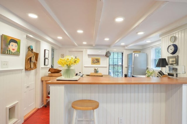 kitchen featuring an AC wall unit, stainless steel refrigerator, beamed ceiling, a kitchen bar, and kitchen peninsula