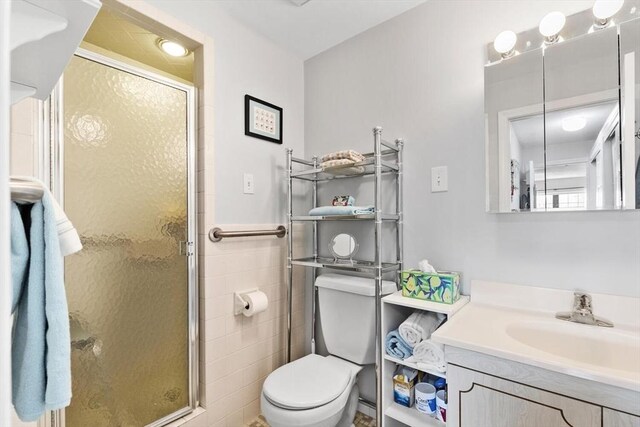 bathroom with vanity, tile walls, toilet, and a shower stall