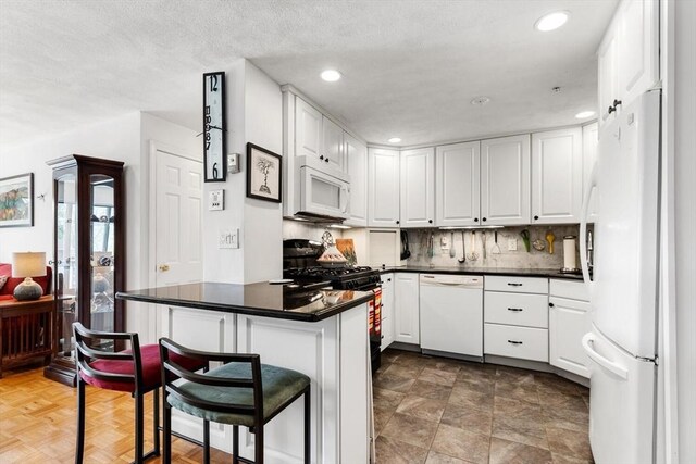 kitchen featuring white appliances, white cabinetry, dark countertops, and a kitchen breakfast bar