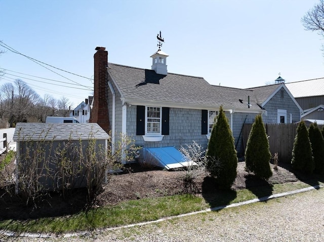 exterior space featuring roof with shingles, fence, and a chimney