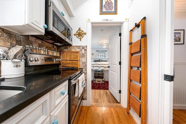 kitchen featuring dark countertops, white cabinetry, light wood-type flooring, appliances with stainless steel finishes, and vaulted ceiling