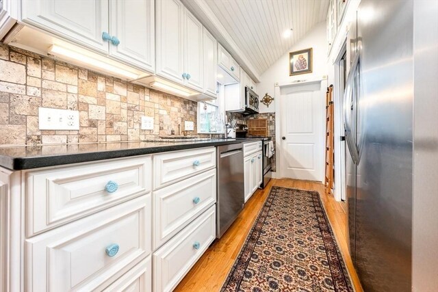 kitchen featuring white cabinets, stainless steel appliances, dark countertops, and light wood-style flooring