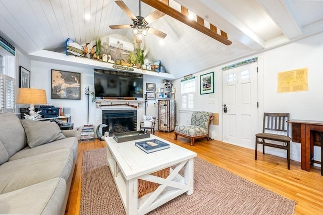 living room with a ceiling fan, a brick fireplace, vaulted ceiling with beams, and wood finished floors