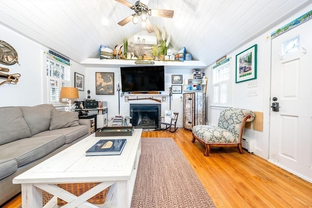 living room featuring wood finished floors, a baseboard heating unit, vaulted ceiling, a fireplace, and a ceiling fan