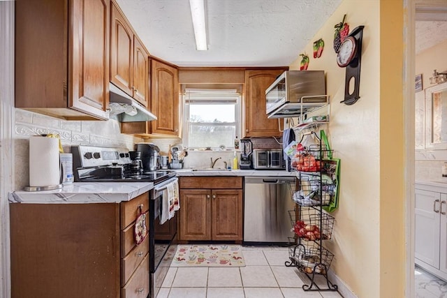kitchen with appliances with stainless steel finishes, light countertops, brown cabinetry, backsplash, and under cabinet range hood
